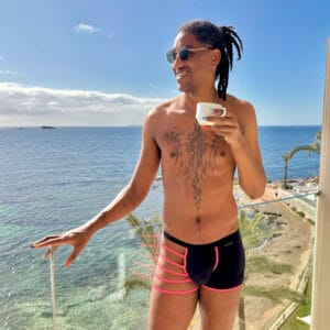 Disfruta de un día soleado en la playa con un hombre con tatuajes, gafas de sol y ropa de baño moder.