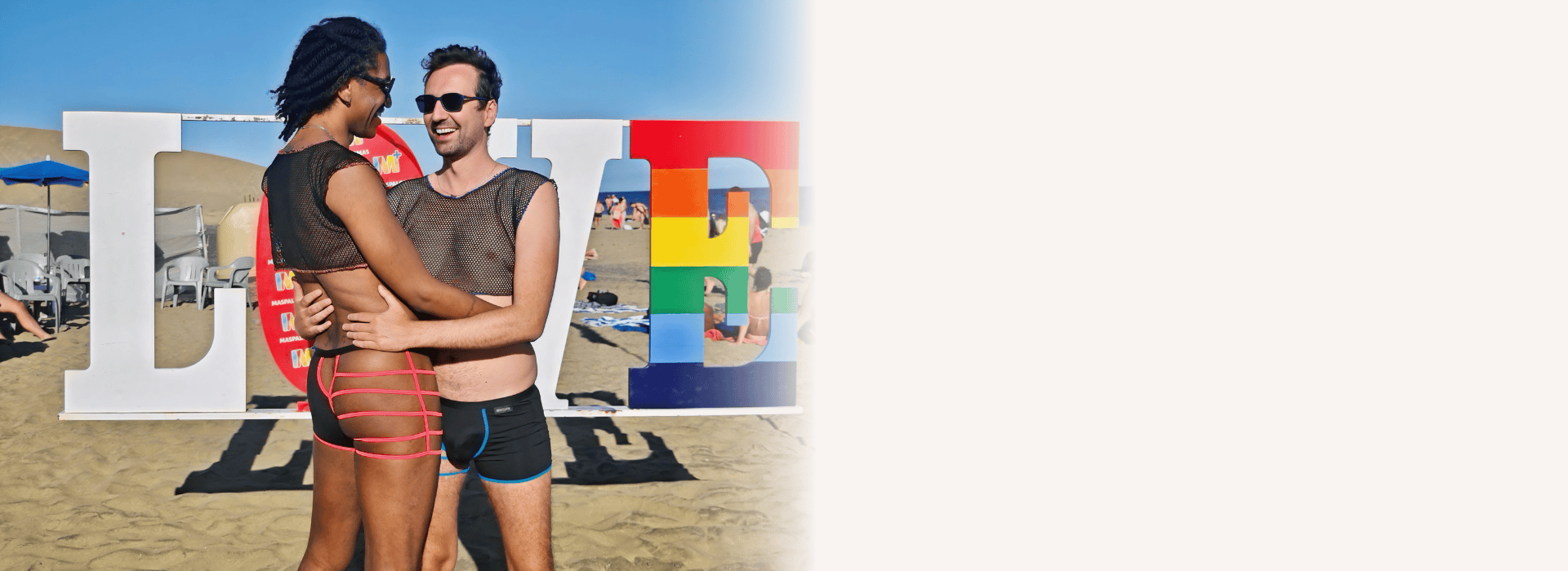 Pareja en la playa con letras grandes de colores en el fondo.